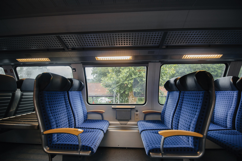 Railcar interior showing blue seating and windows surrounded by rail interior plastics
